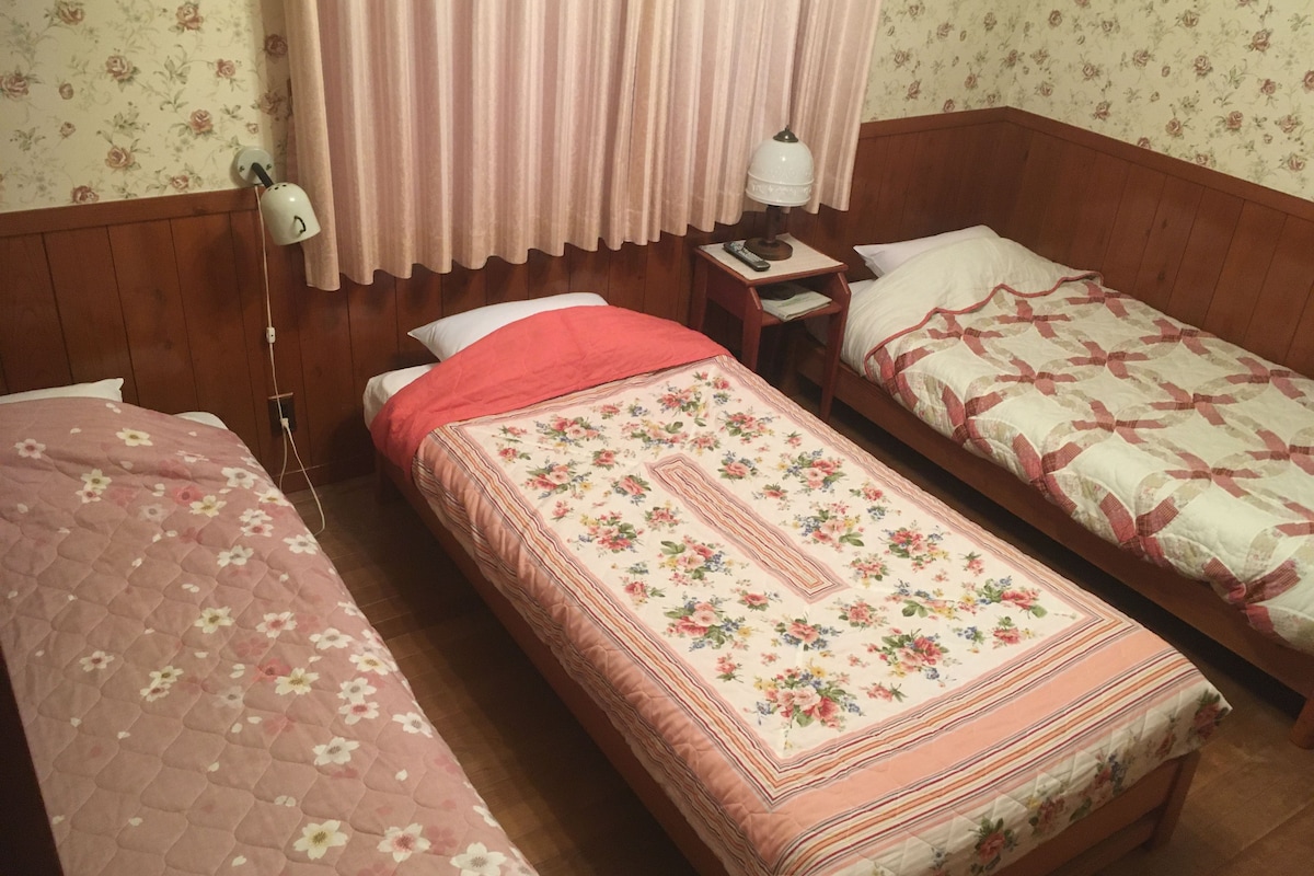A room with two single beds, a nightstand, a lamp, and a wall clock.