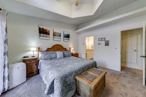 Une chambre à coucher comprenant un lit, des tables de chevet, une commode, un banc en bois et une porte donnant sur une autre pièce.