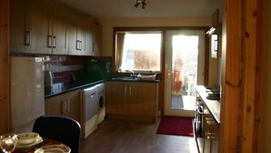 Cocina compacta con muebles de madera, lavadora y comedor con mesa para dos.