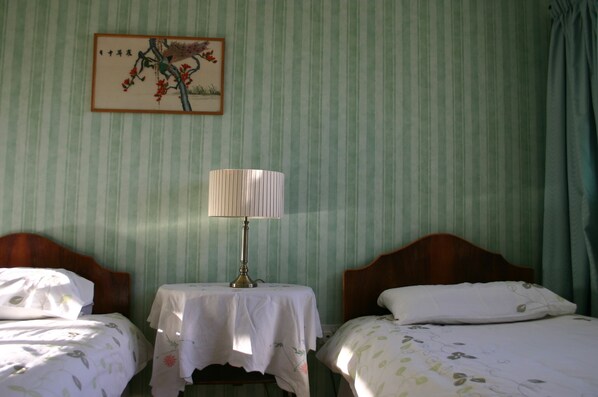A room with two beds, a table with a lamp, and a painting on the wall.