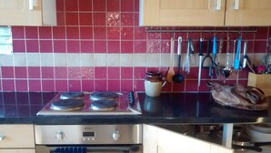 Una cocina con salpicadero de azulejos rojos y blancos, una estufa y varios utensilios de cocina colgados en la pared.