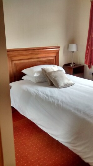 A neatly made bed with white linens and pillows, a wooden headboard, and a red carpeted floor.