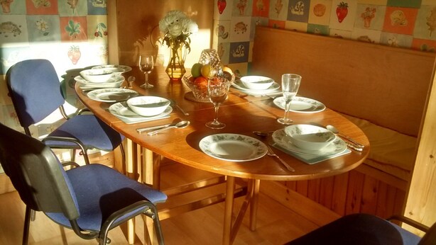 Una mesa de comedor dispuesta con platos, fuentes, cubiertos y vasos, rodeada de sillas azules.
