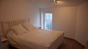 A bedroom with a bed, a nightstand, a window, and a door. - The edge of Saint Quentin 10 minutes from METZ at the foot of Mont Saint Quentin (Lessy)