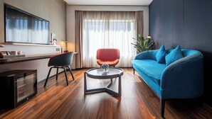 A modern living room with a blue sofa, a red chair, a glass coffee table, a flat-screen TV, and a large window with curtains. - Holiday Inn Express Shenzhen Dongmen by IHG (Shenzhen)