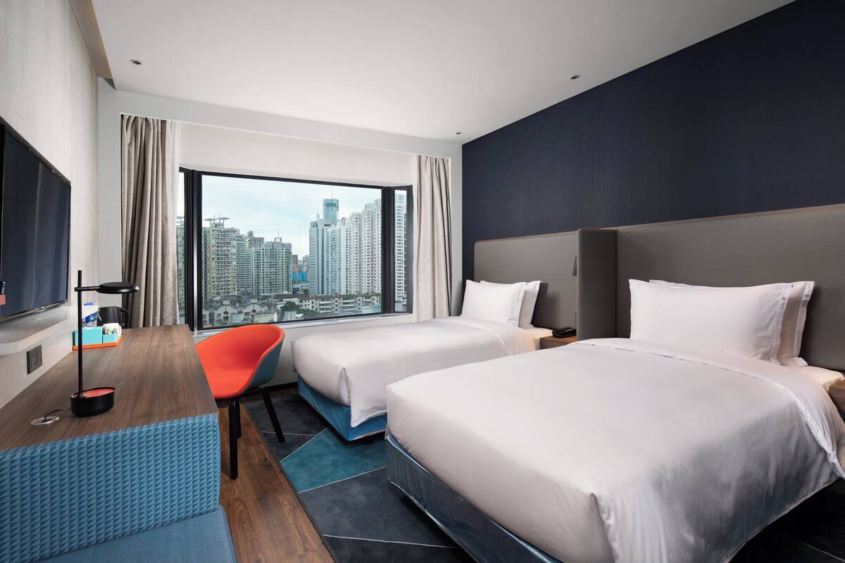A hotel room with two beds, a TV, a desk, and a chair.