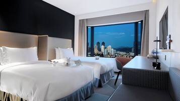 Habitación de hotel con dos camas, un escritorio y un ventanal grande con vistas a la ciudad.