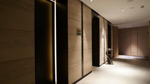 A corridor with a modern design, featuring a combination of wooden and black panels, a small table, and an elevator. - Holiday Inn Express Shenzhen Dongmen by IHG (Shenzhen)