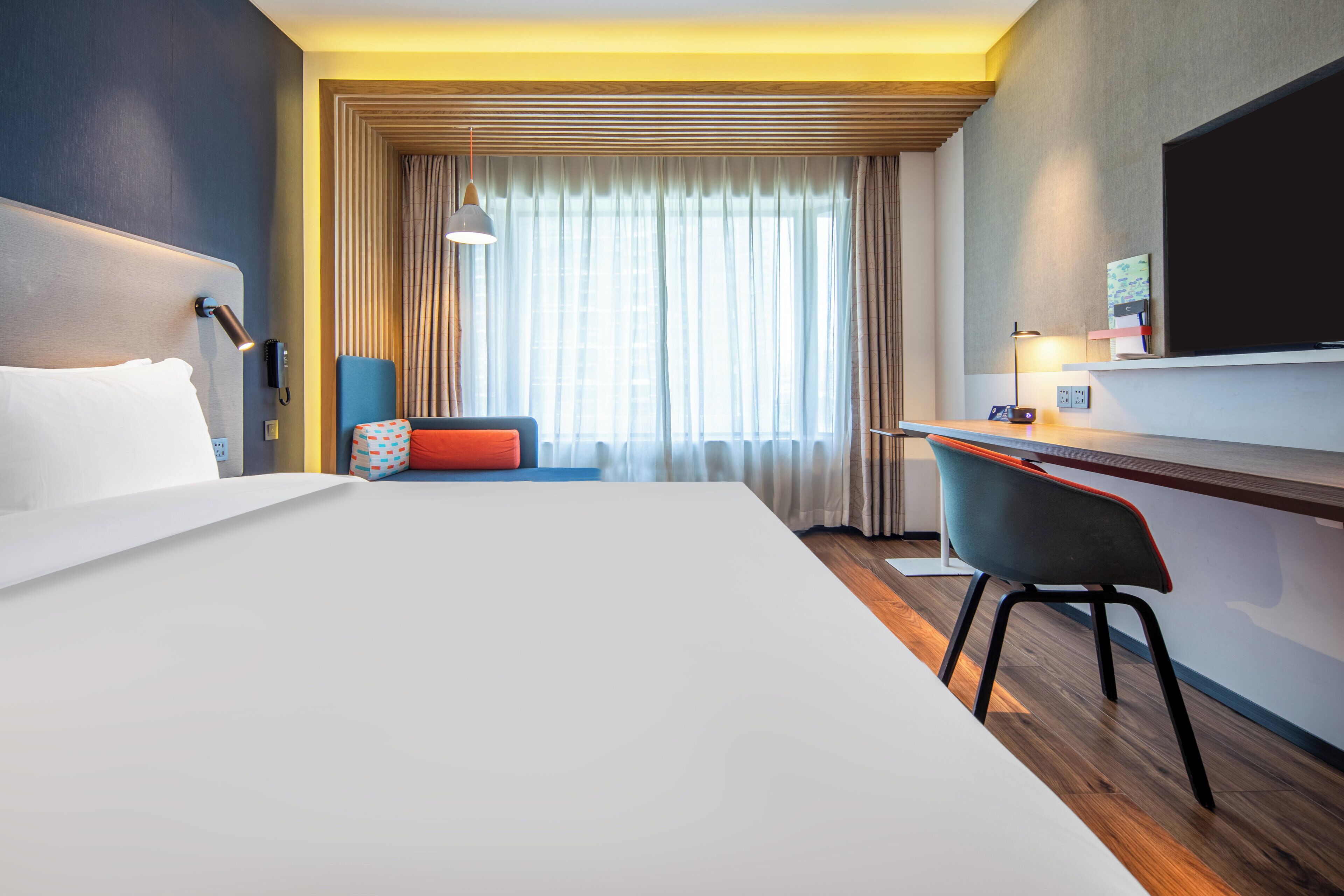 A hotel room with a large bed, a desk, a chair, a TV, and a window with curtains.
