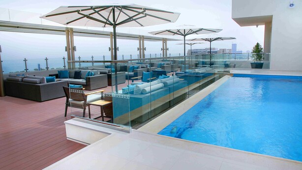 Un espace piscine aménagé sur le toit, doté de rampes en verre, de chaises longues et de parasols.