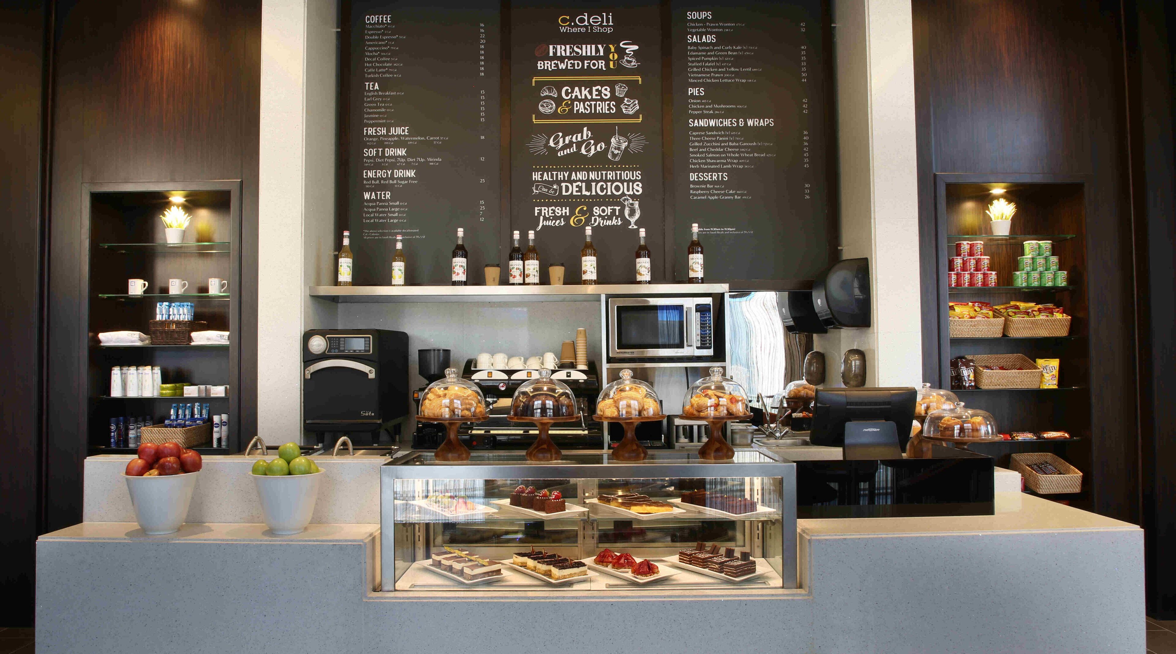 A cafe counter with a menu board, coffee machines, and a display of pastries and desserts.