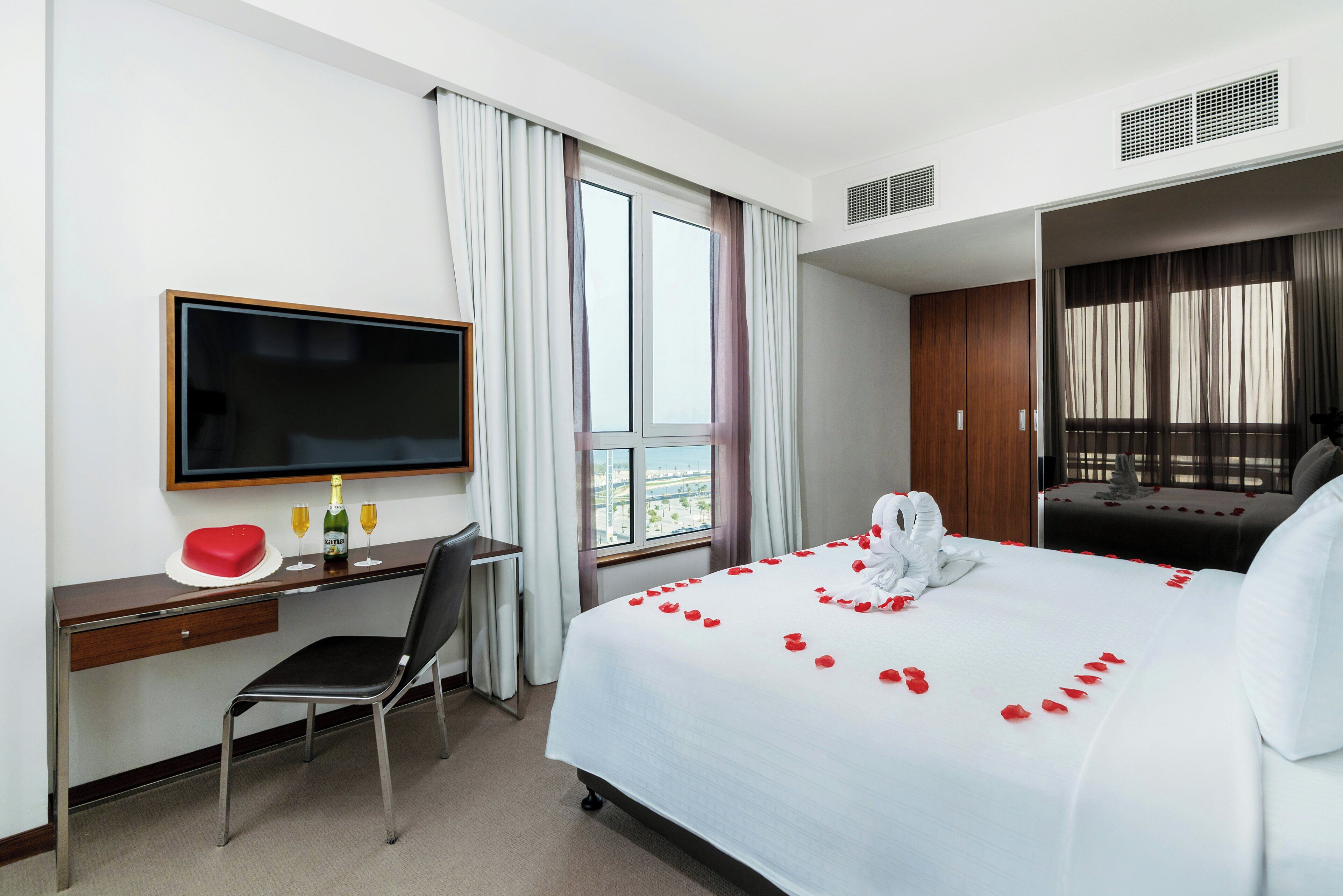 A hotel room with a bed, a desk, a chair, a TV, and a window.