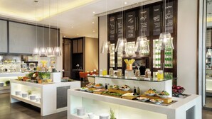 Un buffet moderne dans un hôtel, avec de nombreux présentoirs de nourriture, des vitrines et des suspensions lumineuses.