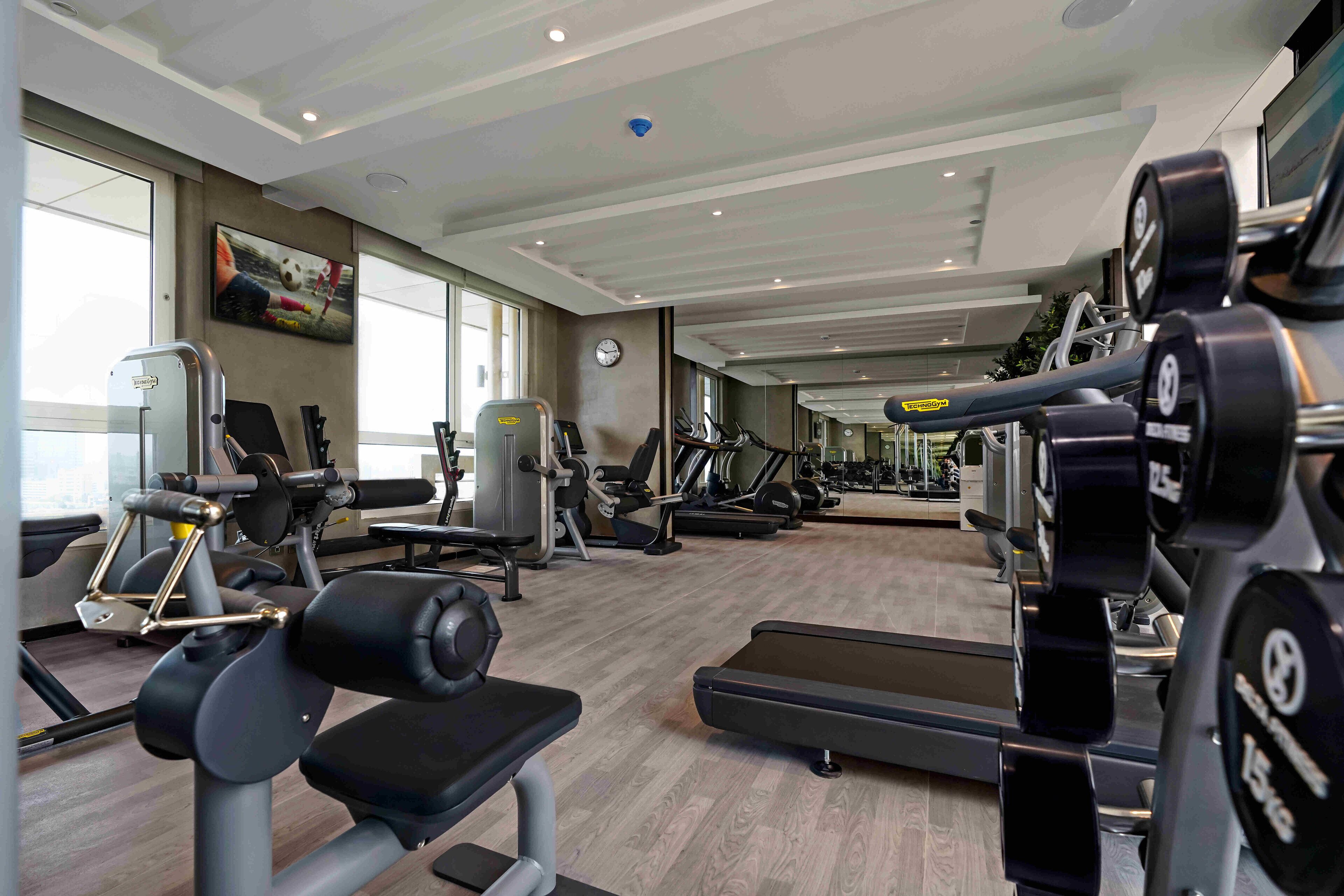 A gym with various exercise equipment, large windows, and a clock on the wall.