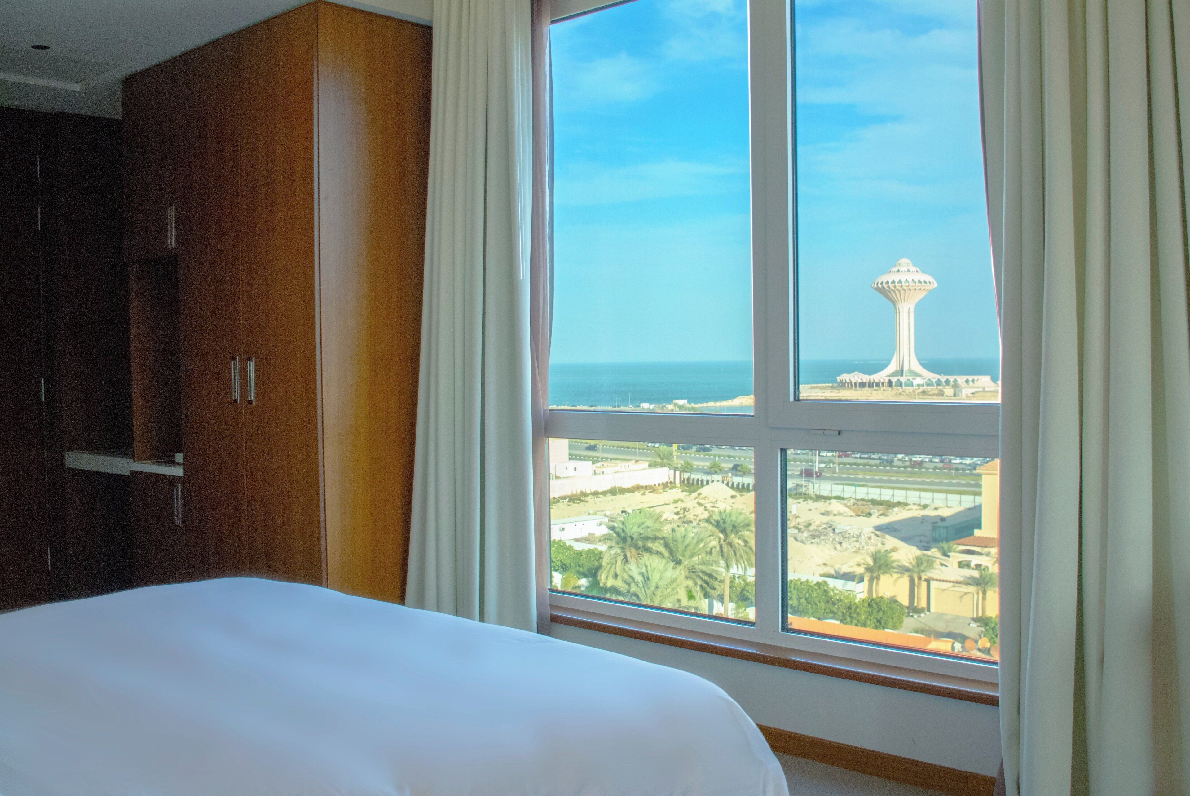 A hotel room with a large window, a bed, and a wardrobe.