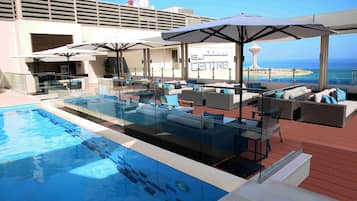 Relax by the pool surrounded by lounge chairs and sofas, with umbrellas providing shade and stunning ocean views.