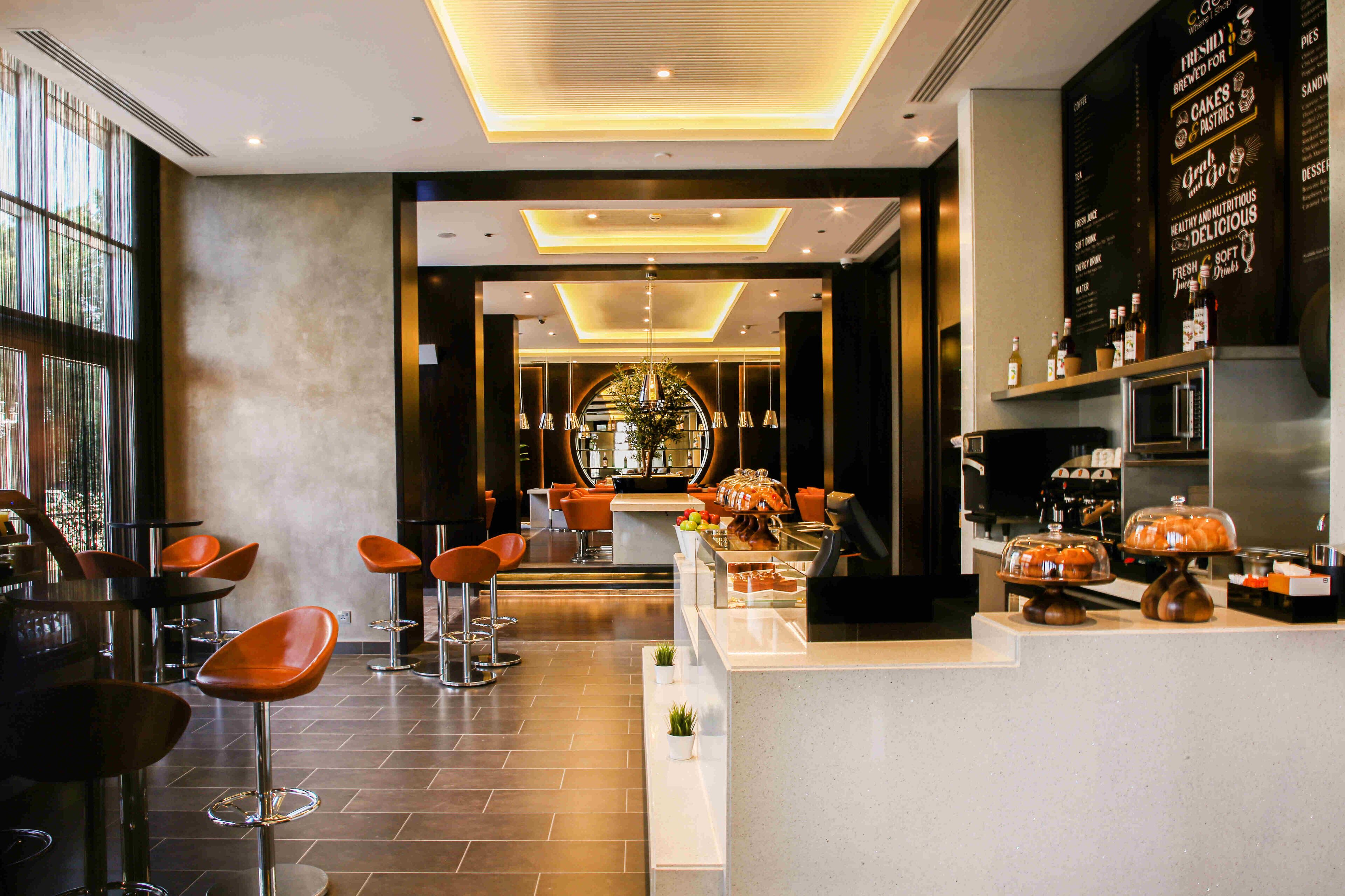 A modern bar area with high stools, a counter with baked goods, and a menu board.