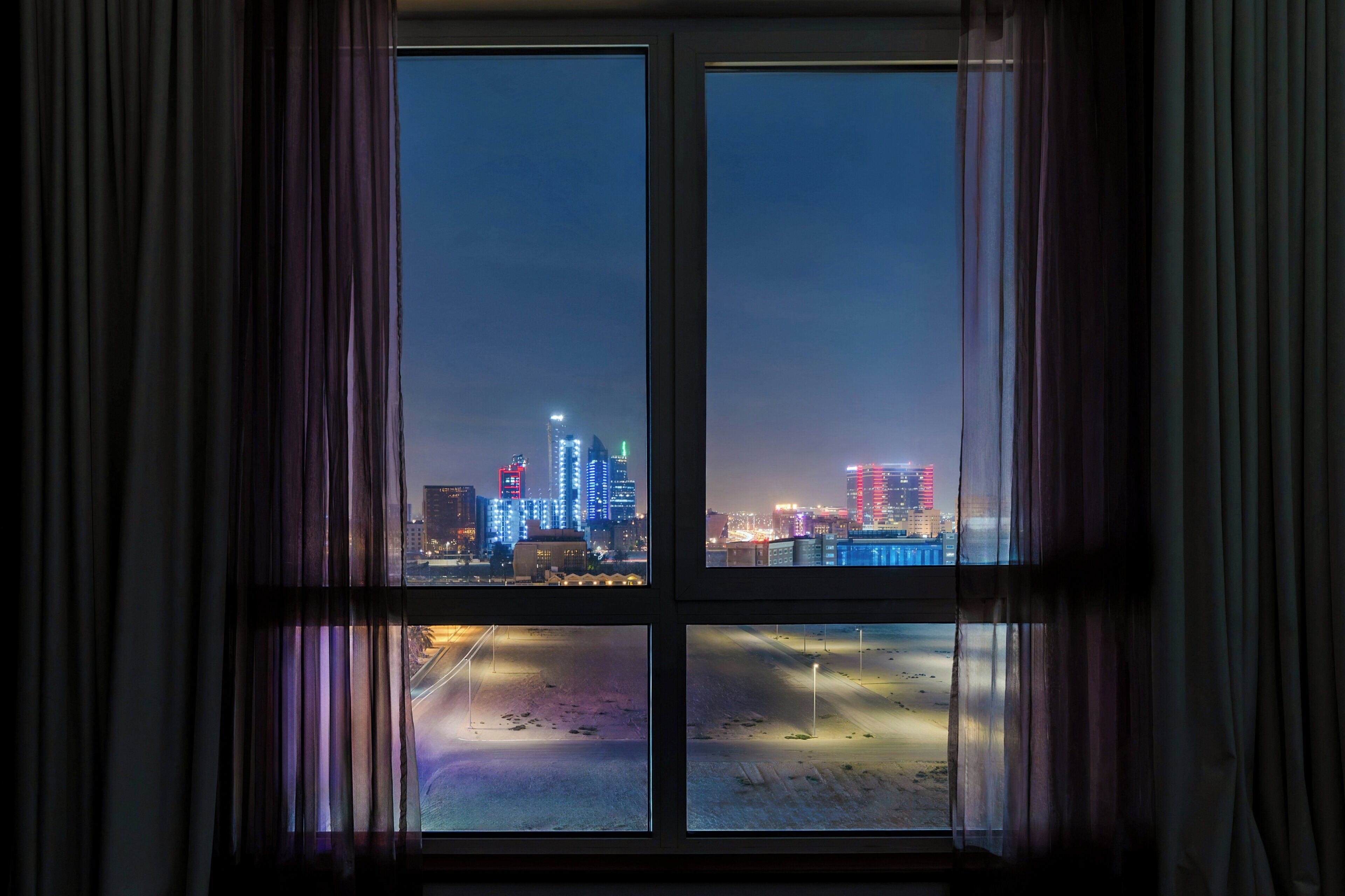 A window with a view of a cityscape at night, including illuminated buildings and a body of water.