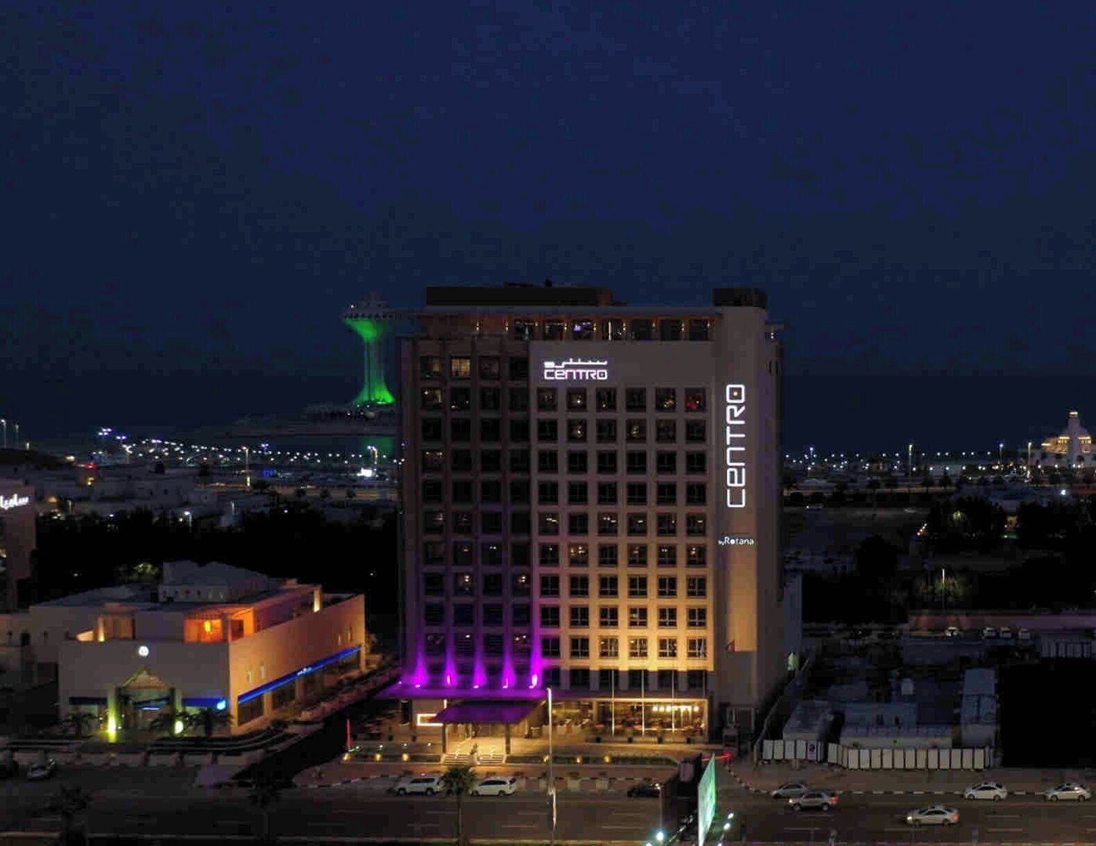 A multi-story hotel with 'CENTRO' signage, a parking lot, and a distant illuminated tower.