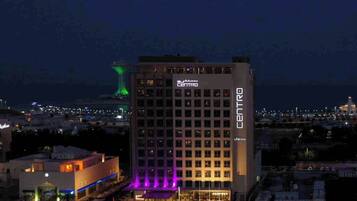 A multi-story hotel with 'CENTRO' signage, a parking lot, and a distant illuminated tower.