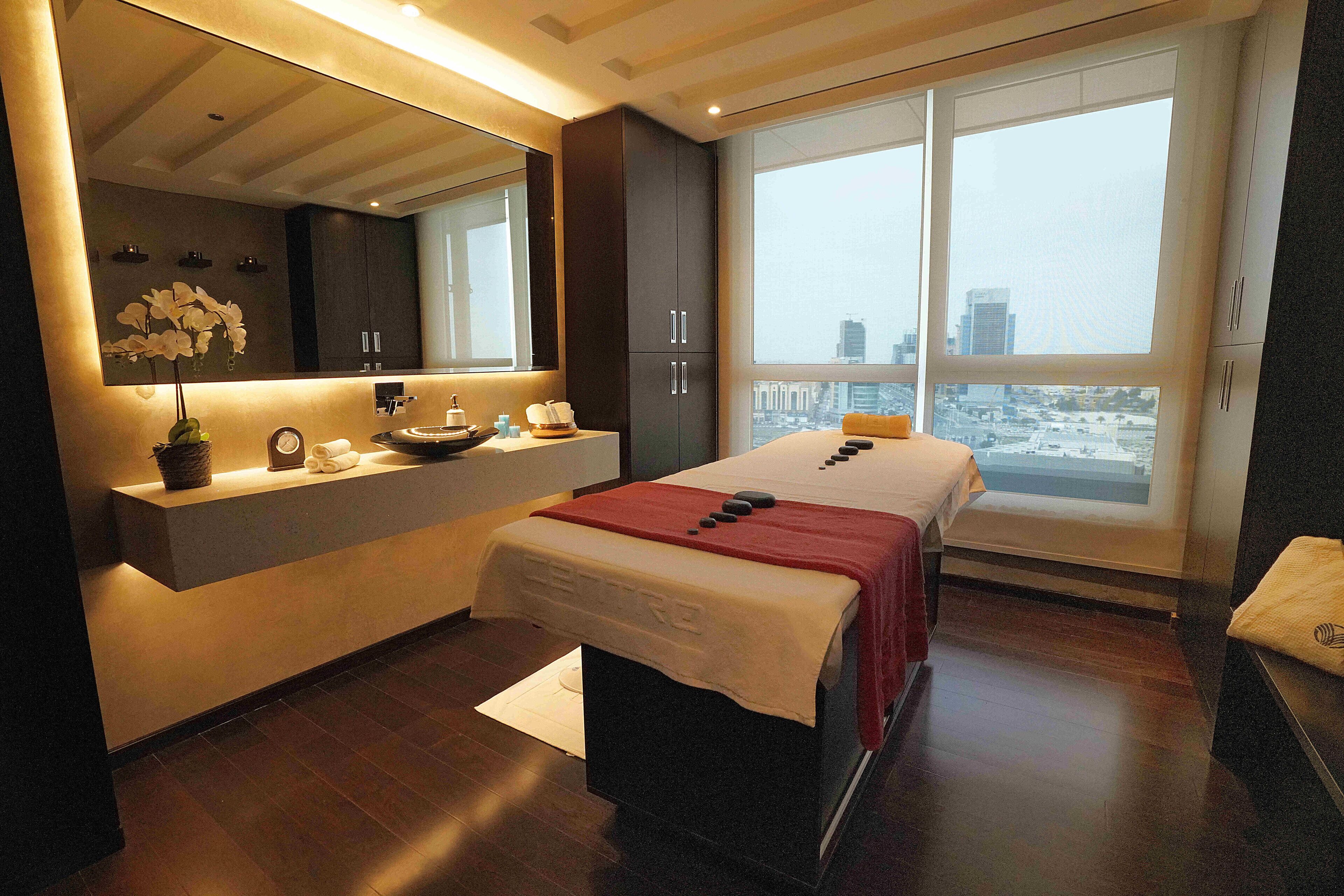 A modern bedroom with a large bed, a bedside table, a mirror, and a city view.