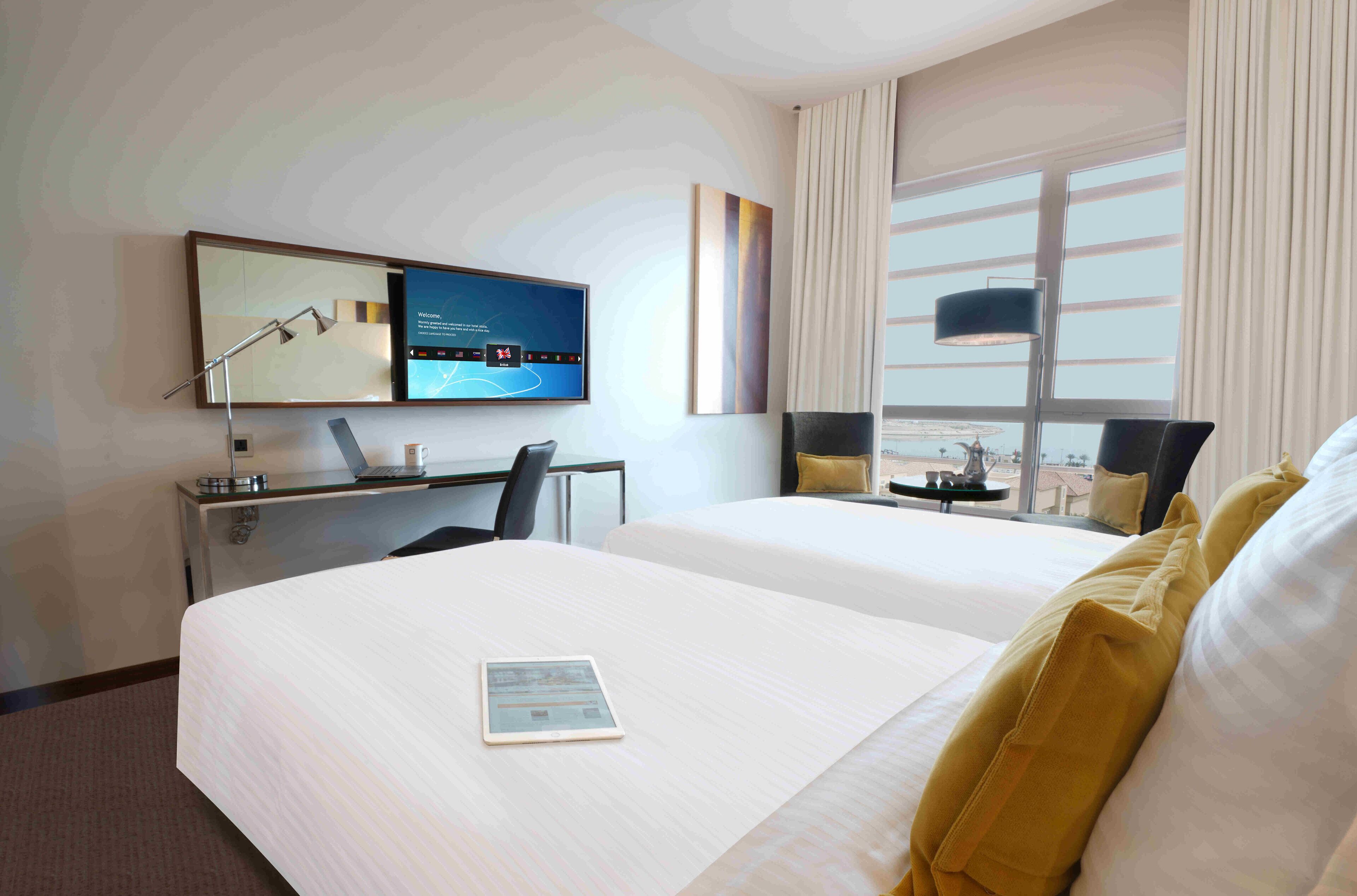 A hotel room with two beds, a desk, a flat-screen TV, and a large window.