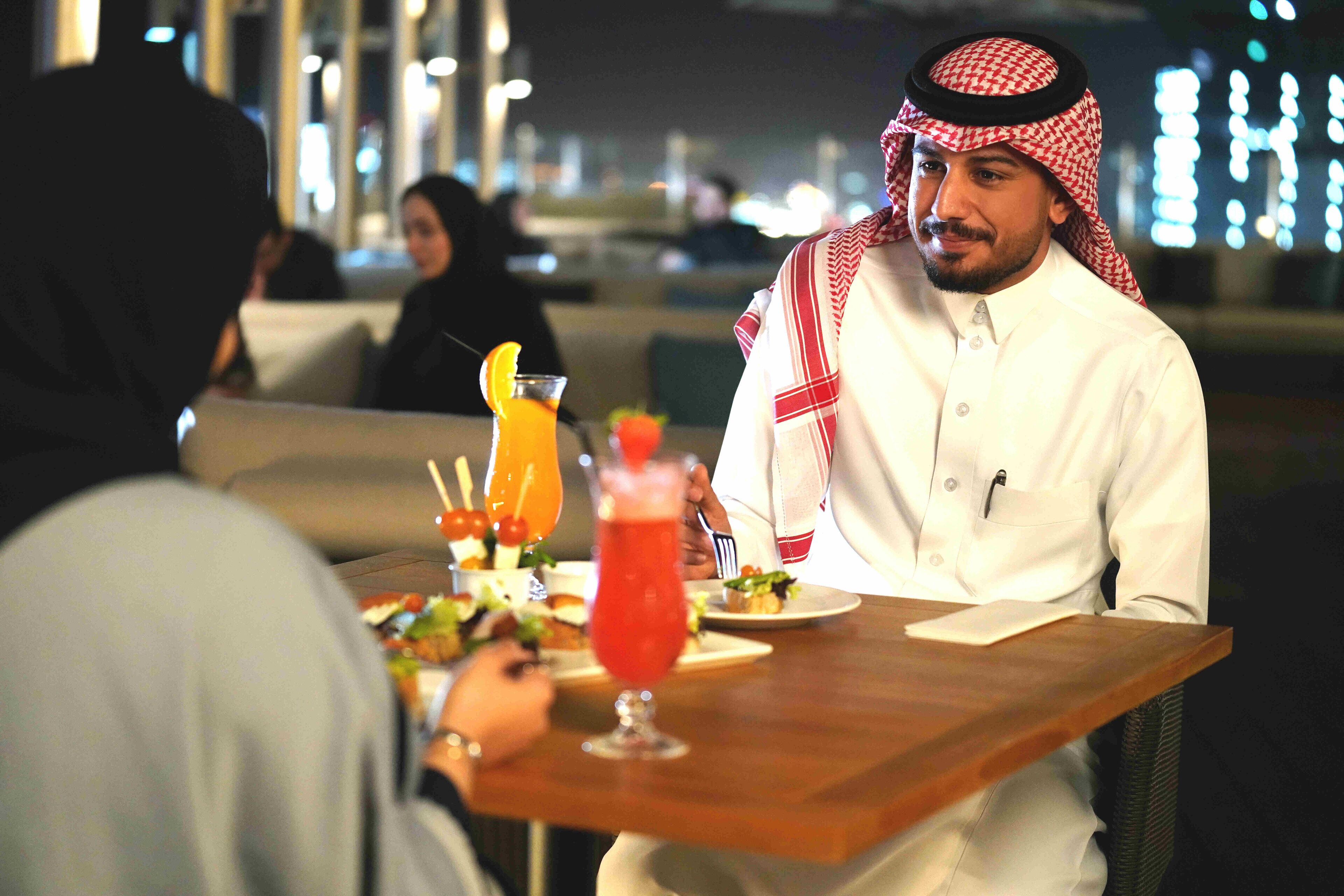 A dining table with a meal, a drink, and a person wearing traditional attire.