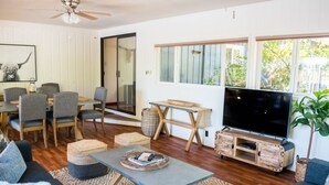 A living room with a sofa, coffee table, TV stand, and dining area with chairs and a table. - Historic Creswell Farmhouse Pool+New Spa - 13 min to Eugene, U of O, & Wineries! (Creswell)