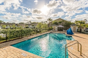 Relax by the pool surrounded by a paved deck and a black fence.