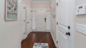 Un pasillo con puertas blancas, una lámpara en el techo, un termostato y un tapete decorativo.