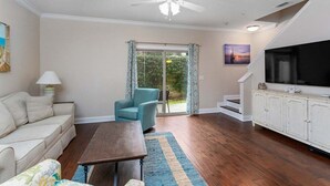 Una sala de estar con un sofá, una silla, una mesa de centro, un televisor y una escalera que lleva a un balcón.