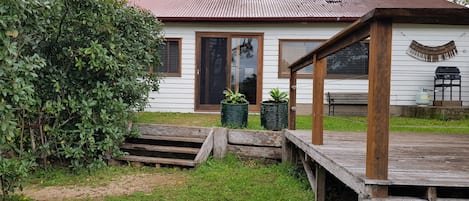 Una casa blanca con terraza de madera, puerta corrediza de vidrio y un pequeño jardín con macetas.