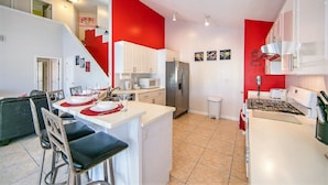 Una cocina moderna con armarios blancos, un refrigerador de acero inoxidable, una estufa a gas y un comedor con una mesa blanca y sillas negras.