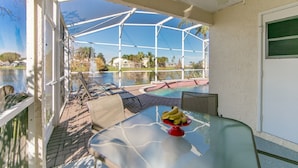 Un espacio al aire libre cubierto con piscina, sillones de descanso y una mesa con fruta.