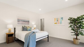 A bedroom with a bed, bedside tables, a wall-mounted painting, a door, and a potted plant. - Coastal Hideaway in Blairgowrie (BLAIRGOWRIE)