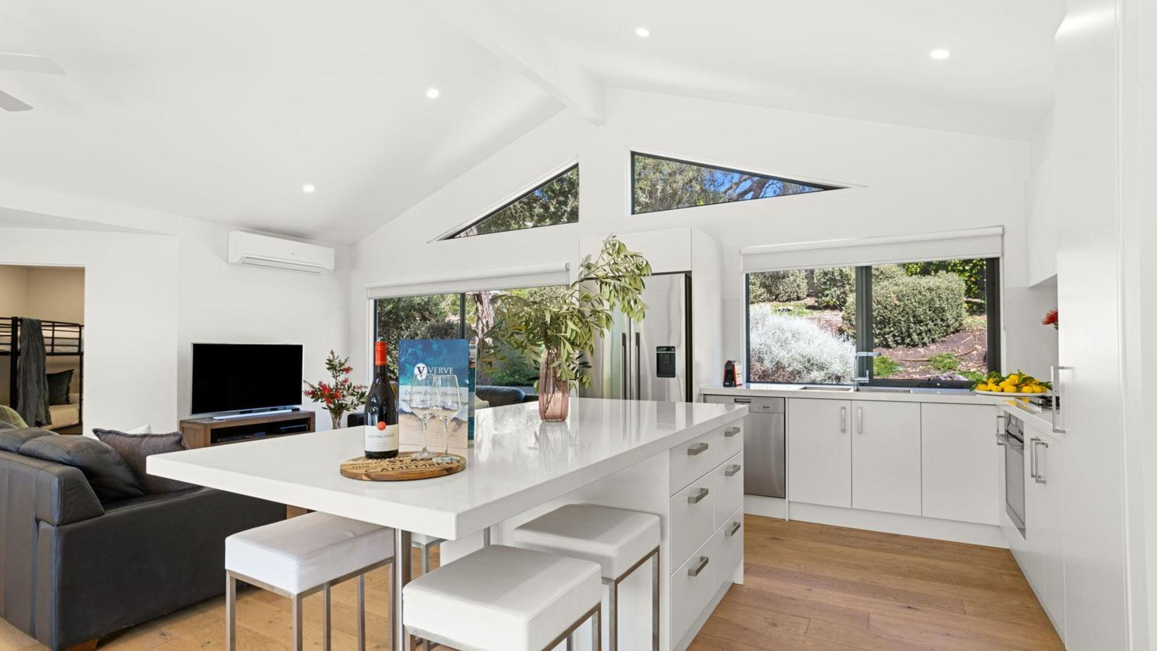 Een moderne keuken met een centraal eiland, witte kasten en een groot raam met uitzicht op groen.