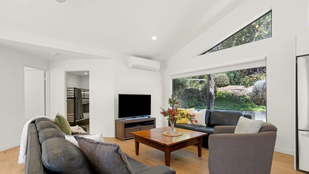 Un salon moderne avec un canapé, une table basse, un téléviseur et une vue sur un jardin grâce à de grandes fenêtres.