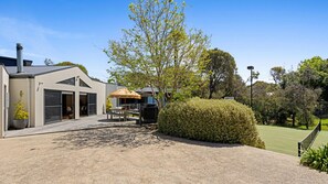 Una casa moderna con un patio, una zona de barbacoa y una cancha de tenis.