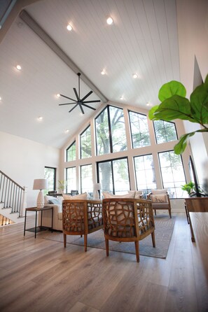 A spacious room with a high ceiling, large windows, and a modern chandelier.