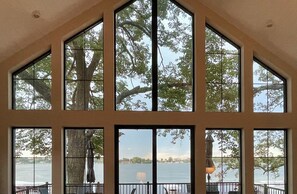 A room with large windows overlooking a body of water, a statue, and a lamp.
