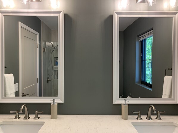 A bathroom with two sinks, each with a mirror above. There is a shower visible in the mirror reflection.