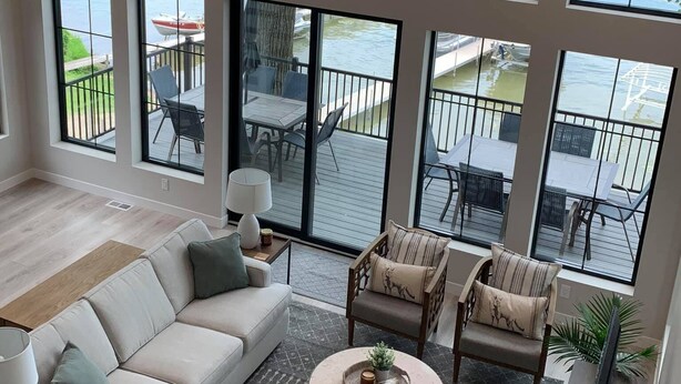 Amplia sala de estar con un ventanal que da a una terraza y vista al agua, un sofá, una mesa de centro y un mueble para el televisor.