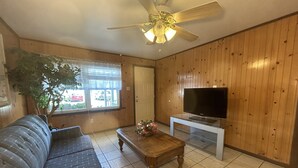 Un salon avec un mur lambrissé en bois, un canapé, une table basse, un téléviseur et un ventilateur de plafond.