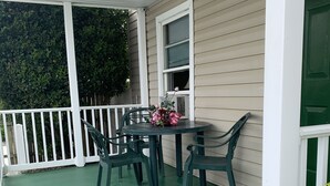 Une véranda avec un sol vert, une table entourée de chaises et une fenêtre agrémentée d’un arrangement floral.