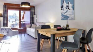A modern living room with a sofa, a dining table with chairs, a large window, and a painting of mountains. - L'Espace Montagne by Interhome (Chamonix)