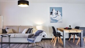 A modern living room with a sofa, a dining table with chairs, a lamp, and a painting of mountains. - L'Espace Montagne by Interhome (Chamonix)