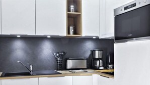 A modern kitchen with white cabinets, a black countertop, a stainless steel toaster, a coffee maker, and a built-in oven. - L'Espace Montagne by Interhome (Chamonix)