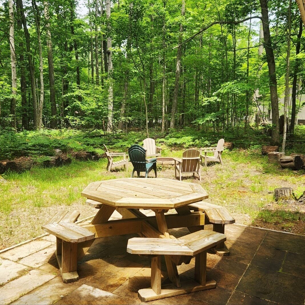 A wooden picnic table with benches in a forested area.