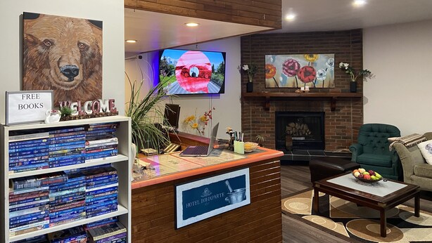 A hotel reception area with a wooden reception desk, a television, a fireplace, and a bookshelf with books. - Ranchland Inn (Nanton)