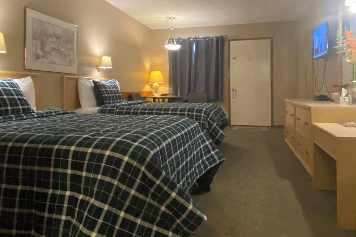 A hotel room with two beds, a desk, a chair, a television, and a door.
